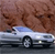 Static image of a silver sedan with a blue roof parked on a gray road against a brown textured background.