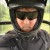 Pixelated image of a person wearing a dark military-style helmet and uniform with a blurred background.
