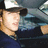 Pixelated image of a person with light brown hair wearing dark clothing and a white cap, set against a blurred background.