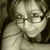 Pixelated grayscale image of a person with short hair wearing glasses and a light-colored shirt, holding an object near their face.