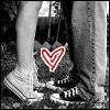 Black-and-white image of two people's legs and feet in sneakers, with a red heart symbol overlaid on the lower center.
