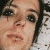 Pixelated close-up of a person's face with dark hair, visible eyes, nose, mouth, and light skin tone against a blurred background.