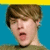 Pixelated close-up of a person with brown hair against blue background, mouth open in mid-expression.