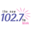 Static pixel art displays '102.7' in blue numerals with pink radiating lines and gray rectangular shapes on a white background.