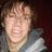 Pixelated image of a person with light brown hair wearing gray clothing against dark red background, next to black with white text