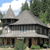 Pixelated image of a house with a sloped roof, surrounded by greenery and trees under a partly cloudy sky.