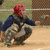 A pixelated figure in a crouched baseball catcher pose with red hair, blue sleeves, and camouflage pants on a field background.