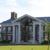 Pixelated image of a white-columned building with a blue roof, dark windows, and a chimney, set against a light sky and green grass.