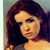 A pixelated close-up of a person with long dark brown hair, wearing a dark top, against a light blue background.