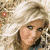 A woman with long blonde hair in a blue top poses against a blurred background, next to a yellow star logo and partial text reading "SqaTer GirL".