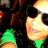 Pixelated close-up of a person with dark hair and light skin wearing green clothing, set against a dark background.