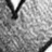 A grayscale pixelated image showing a partial view of a dark curved shape against a light background with scattered darker pixels.