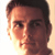 Pixelated close-up of a person's face with short dark hair, visible eyes, nose, mouth, and ear against a light background.