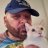 A pixelated static image shows a person wearing a dark blue cap and a striped shirt holding a small white dog with dark eyes and nose.