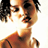 Pixelated static image of a person's face and upper torso with brown hair, visible facial features including eyes, nose, mouth, and neck, wearing an orange-brown garment with dark straps or lines on the shoulder area.