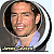 Pixelated portrait of a smiling person with short dark hair, wearing a light blue shirt and patterned tie against a gray circular background.