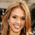 A pixelated close-up of a smiling person with light brown hair, wearing a dark top against a blurred background.