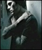 A grayscale animated sequence shows a person with long dark hair in a dimly lit room, arms crossed over chest, shifting posture slightly between frames.