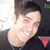 Pixelated static image of a smiling person with short dark hair wearing a black top, featuring visible dithering and compression artifacts on a white background.