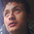 Pixelated close-up of a person's face with light skin tone, dark hair, and visible eyes, nose, and mouth against a dark background.