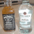 Two bottles with orange caps and white labels sit side-by-side on a light surface, one bottle appears slightly blurred in the second frame.