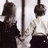 Two pixelated figures stand side-by-side in a grayscale scene with a vertical pole, while white pixelated text appears on a black background.