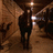 A dark silhouette of a figure in a dimly lit tunnel with diagonal lines and bright lights at the far end, viewed from multiple angles.