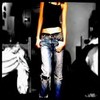 A person in a black crop top and light blue jeans stands against a dark background with partial side views of other figures.