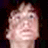 Pixelated static image of a human face with light skin tone against dark background, likely from low-resolution source material or intentional pixelation effect.