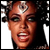 Pixelated close-up of a person with dark curly hair, wearing a silver headpiece and red lipstick, mouth open in an expressive pose.