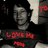 Pixelated grayscale portrait of a person with dark hair and neutral expression, overlaid with red text reading 'LOVE ME' on black background.