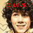 Pixelated image of a person with curly dark hair and light skin, wearing a light-colored patterned top, with red text above the head.