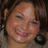 Pixelated close-up of a smiling person with light brown hair, visible ear, and dark background.