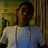 Pixelated image of a person in profile wearing light blue and white clothing against a blurred background with green, yellow, and brown tones.