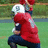 Pixelated image of a football player in red jersey and white helmet crouching on grass field with text overlays.