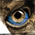 A close-up of a pixelated eye with a brown iris, blue highlights, and a black pupil, set against a blurred brown and beige background.