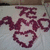 A static image of a heart-shaped arrangement of red petals on a white surface with the text 'Te Amo' above it.
