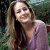 A pixelated image of a person with long brown hair wearing a light purple top against a blurred green background, next to bright green text on dark green.