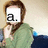 Pixelated image of a person with brown hair and beard wearing green clothing, holding hand near face, white square overlay with black 'a.' text on left side.