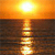 A static pixelated image of a bright sun setting over a dark body of water, with the sun's reflection creating a vertical light path on the water's surface.