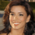 A pixelated close-up of a person with brown hair, light skin, and a smiling expression, wearing a dark top against a blurred background.