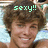 Pixelated image of a person with brown curly hair and light skin, wearing a dark top, with green text reading 'sexy!!' overlaid above the head.