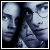 Pixelated static image of two overlapping faces with dark hair and light skin tones, rendered in blue-gray palette against a white background.