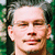 A pixelated portrait of a man with dark hair and glasses, showing three variations in facial expression against green foliage background.