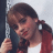 Pixelated image of a person with brown hair in pigtails holding a dark microphone, wearing red and white clothing against a light background.