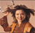 A pixelated figure with dark hair wears an orange garment and raises a hand near their head against a light brown background.