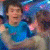 repeated figures in blue shirts dancing with others against a colorful, blurred background