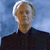 Pixelated image of a person with light-colored hair wearing a dark shirt against a blue gradient background.