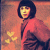 Pixelated image of a person with short dark hair wearing a red garment against an orange background, holding yellow flower-like shapes.