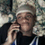 Pixelated static image of a person with light brown hair wearing a white headband, dark shirt, and blue-and-white striped sleeves, holding a microphone near their mouth.